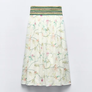 Blommig långkjol med broderad midja - Superfin långkjol med ett blommigt mönster i pastellfärger. Kjolen har en broderad midja i grönt, gult och svart som ger en snygg kontrast. Perfekt för sommarens alla tillfällen! 🌸