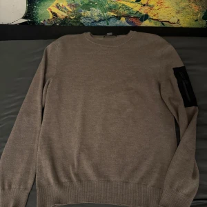 Beige tröja från Snoot - Säljer en snygg beige tröja från Snoot i storlek L. Den har en cool svart detalj på ärmen med dragkedja och knapp. Perfekt för höst och vinter, och den är supermjuk och bekväm. Passar både till vardags och lite finare tillfällen. 🧥✨