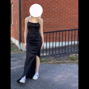 Svart långklänning med öppen rygg - Säljer en svart långklänning med smala axelband och en snygg öppen rygg med snörning. Klänningen har en slits framtill. Perfekt för festliga tillfällen! 🖤.    Nypris 999kr