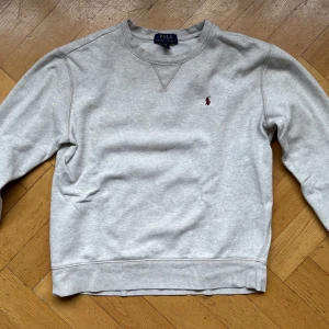 Grå sweatshirt från Polo Ralph Lauren - Säljer en klassisk grå sweatshirt från Polo Ralph Lauren i storlek L/G (14-16). Tröjan har en broderad röd logga på bröstet och är i mycket bra skick.