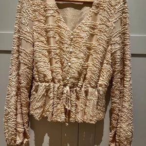 Blus / Topp - En fin topp med fina knappar framtill , armarna är luftiga och med resår band kring handleden .  Färgen är aprikos 