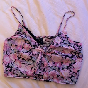 Croppat blommigt linne med knytdetalj - Ett blommigt croppat linne med en knytdetalj framtill från divided by H&M. Väldigt fint på sommaren men har tyvärr blivit för litet för mig! Använt en del men har inga defekter. 🌸