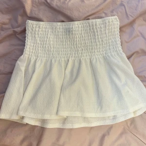 Vit kjol från Gina Tricot - Superfin vit kjol från Gina Tricot i storlek L. Den har en smockad midja som ger en bekväm och flexibel passform. Perfekt för sommardagar eller en avslappnad vårlook. Kjolen är kort och har en luftig känsla, vilket gör den idealisk för varmare väder.