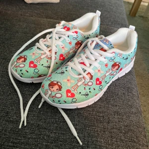 Färgglada sneakers med barnmotiv - Säljer ett par unika och färgglada sneakers i storlek 39. Skorna har ett lekfullt mönster med medicinska figurer i olika färger som rött och blått på en ljusblå bakgrund. De är helt nya och har vita snören. Perfekta för någon som vill ha ett par roliga och bekväma skor!