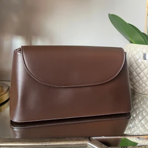 Brun axelväska i skinn - Snygg brun axelväska i skinn med enkel och stilren design. Väskan har en slät yta och en praktisk axelrem som kan justeras. Perfekt för både vardag och festliga tillfällen. Den är i mycket bra skick och redo att användas direkt!