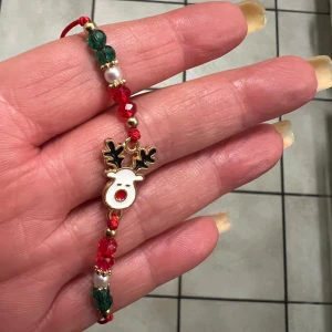 Juligt armband med renmotiv - Superfint armband med ett gulligt renmotiv i mitten. Armbandet har pärlor i rött, grönt och guld samt små vita pärlor. Perfekt accessoar för julen och ger en festlig touch till din outfit. Justerbar storlek så det passar de flesta handleder.