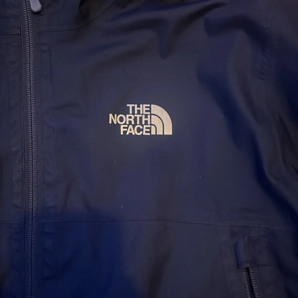 Säljer en svart vindjacka från The North Face i bra skick. Jackan har en huva och dragkedja framtill, perfekt för blåsiga dagar. Den är stilren och funktionell med två praktiska fickor med dragkedja. Passar både till vardags och utomhusaktiviteter.. Jackor.