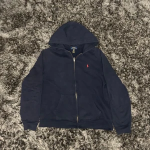 Mörkblå hoodie från Polo Ralph Lauren (XL barn) - Säljer en snygg mörkblå hoodie från Polo Ralph Lauren i storlek XL (barn) . Den har en dragkedja framtill och en klassisk huva. Perfekt för kyliga dagar och passar till både vardag och avslappnade kvällar.