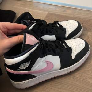 Säljer ett par Nike Air Jordans i svart, vitt och rosa. Skorna är i mycket bra skick och har en snygg rosa swoosh på sidan. Perfekta för både vardag och fest! De har snörning och en klassisk design som aldrig går ur stil.