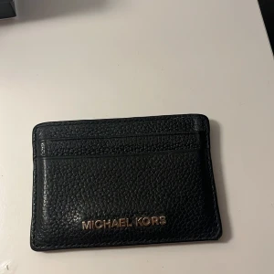 Svart plånbok från Michael Kors - Säljer en stilren svart plånbok från Michael Kors i skinn. Den har en enkel och elegant design med plats för kort. Perfekt för att hålla ordning på dina kort med stil. Passar både till vardag och fest!