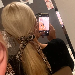 Hårsnodd med ormmönster - Säljer en superfin hårsnodd med ormmönster i beige och svart. Den har en snygg rosett som ger en extra touch till din frisyr. Perfekt för att piffa upp en enkel hästsvans eller fläta. Passar både till vardags och fest!