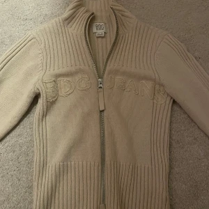 Beige stickad tröja från BDG - Säljer en snygg beige stickad tröja från BDG köpt från Urban Outfiters med dragkedja framtill. Tröjan har ribbade detaljer och texten 'BDG JEANS' broderad på bröstet. Perfekt för höst och vinter. Köpte för 600 kr nypris o säljer för 350 kr. Knappt använd❤️kom privat för mer info❤️