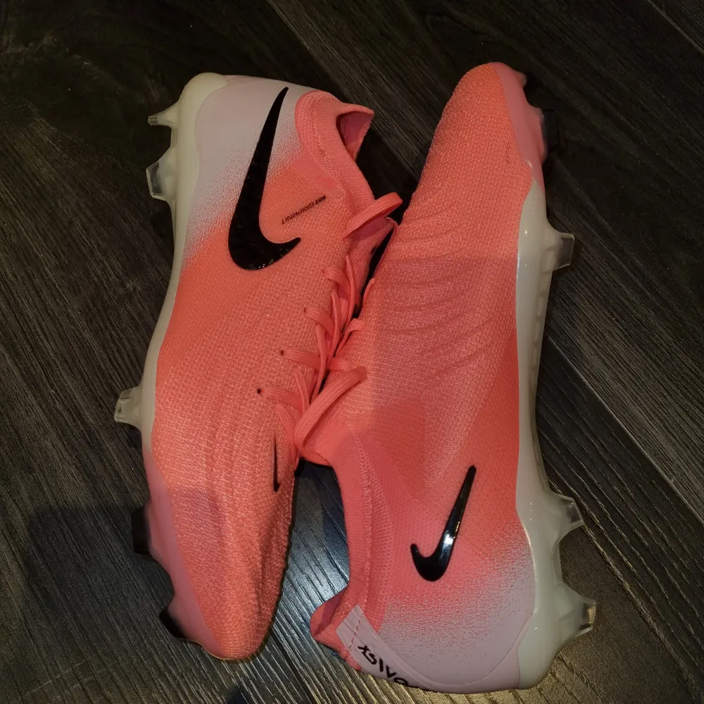 Säljer ett par snygga rosa fotbollsskor från Nike i nytt skick. De har en stilren design med svarta detaljer och snörning för perfekt passform. Perfekta för fotbollsträning eller match. Skorna är lätta och bekväma, vilket ger bra grepp på planen. Storlek 42 skriv för med info.. Skor.