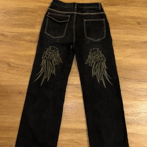 Svarta jeans med broderade detaljer - Svarta jeans med coola broderade vingdetaljer på baksidan och framsidan. Storlek xs men baggy så det passar s/m skulle jag säga🖤 innerbenslängden: Ca 70cm, men de ska hänga lite så det blir längre 