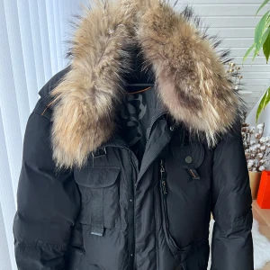 Svart vinterjacka med päls från Hollies - Säljer en snygg svart vinterjacka från Hollies i storlek 54. Jackan har en stor, fluffig päls på kragen och flera praktiska fickor med dragkedja. Perfekt för kalla vinterdagar! 🖤