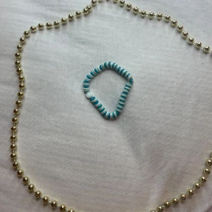 Turkost och vitt armband med smiley - Säljer ett supergulligt armband i turkost och vitt med en liten smiley-detalj. Perfekt för att liva upp vilken outfit som helst! Armbandet är elastiskt och passar de flesta handleder. Perfekt accessoar för sommarens alla äventyr! 🌞