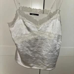 Vit linne med spetsdetaljer från Ginatricot - Säljer ett superfint vitt linne från Ginatricot med spetsdetaljer vid halsringningen och axelbanden. Perfekt för sommardagar eller som ett lager under en kavaj. Linnet har en mjuk och skön känsla, perfekt för både vardag och fest.