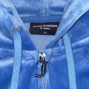 Velour zip up hoodie från Juicy Couture i färgen Ragatta - Säljer en supermjuk och snygg velour zip up hoodie från Juicy Couture i storlek XS färgen Ragatta. Jackan har en dragkedja med ett coolt J-format hänge och justerbara snören i huvan. Perfekt för en avslappnad och stilren look! Nypris: 1300kr, säljer för 750kr. Väldigt bra skick!