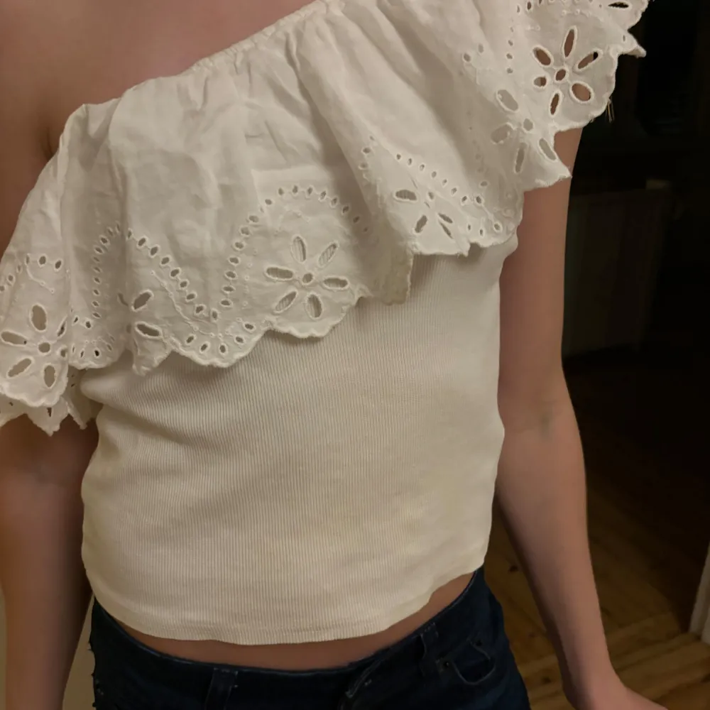 Säljer en superfin vit offshoulder topp med spetsdetaljer. Den har en volangkant som ger en romantisk touch och är perfekt för sommardagar. Toppen är ribbad och sitter tight, vilket gör den både bekväm och stilren. Passar perfekt till både jeans och kjol!. Toppar.