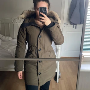 Victoria parka med päls från Canada Goose - Säljer en snygg brun parkajacka från Canada Goose i mycket bra skick. Jackan har en mysig pälsfodrad huva och stängs med både dragkedja och knappar. 