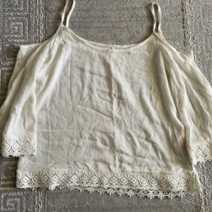 Vit ärmlös topp med spetsdetaljer - Säljer en söt vit ärmlös topp med tunna axelband och vacker spetsdetalj längs nederkanten. Perfekt för sommardagar eller en avslappnad fest. Toppen är i bra skick och passar till både jeans och kjol.