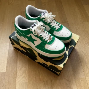 Gröna och vita sneakers från Bape - Säljer ett par snygga gröna och vita sneakers från Bape i mycket bra skick. De har en cool stjärndetalj på sidan och kommer med originalkartong och dustbag. Perfekta för att sticka ut i mängden med sin unika design och färgkombination. Storlek 10,5 US, ca 44,5 EU. 