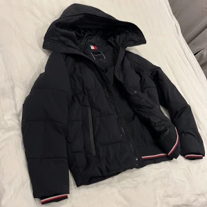 Svart pufferjacka från Tommy Hilfiger - Säljer denna svarta Tommy Hilfiger jackan som är perfekt nu till vintern, har själv beställt en annan jacka då denna är en gnutta för stor på mig (enligt mig) och då ja förmodligen inte kommer använda denna nå mer så får den gå vidare. Nypris: 3100