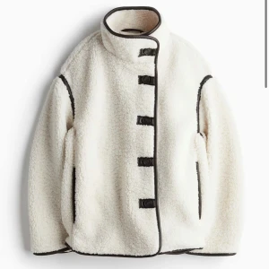 Vit teddyjacka med bruna detaljer - Säljer en supermysig vit teddyjacka med bruna kantdetaljer och knäppning. Jackan har en hög krage och är perfekt för kyliga dagar. Den är både stilren och jätte varm, vilket gör den idealisk för höst och vinter. Passformen är normal och den har långa ärmar.