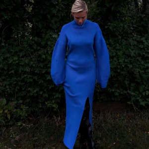 Blå stickad klänning från NA-KD - Säljer en superfin blå stickad klänning från NA-KD med lång ärm och hög krage. Den har en elegant slits framtill och är perfekt för höst och vinter. Klänningen är  uanvänt. Storlek S/M