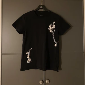 Marc Jacobs T-shirt  - Svart Marc Jacobs T-shirt med snygga detaljer. Fått några mini hål som visas på bilderna, tre jättesmå nära kragen och en lite längre ned.