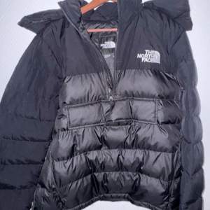 Säljer en svart dunjacka från The North Face i mycket bra skick. Jackan har en halv dragkedja framtill och en stor ficka med dragkedja på magen. Perfekt för kalla vinterdagar med sin varma och puffiga design. Huvan är justerbar och ger extra skydd mot kyla. Passar både till vardags och utomhusaktiviteter.