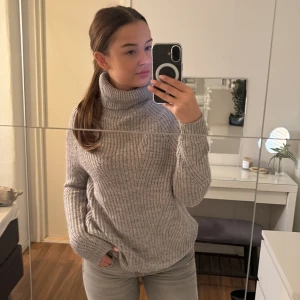 Grå stickad polotröja - Mysig grå stickad polotröja perfekt för kyliga dagar. Den har en hög polokrage och långa ärmar, vilket gör den superbekväm och varm. Perfekt för både höst och vinter. Passar bra till jeans eller leggings för en avslappnad look.