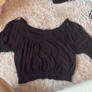 Svart offshoulder topp - Säljer en snygg svart offshoulder topp i mycket bra skick. Toppen är kortärmad och gjord i ett mjukt material.