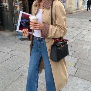 Beige trenchcoat med rutigt foder - Säljer en snygg beige trenchcoat med ett stilrent rutigt foder. Jackan har långa ärmar och klassisk krage. Perfekt för höst, vår och vinter då den är varmfodrad. Den är även omvändningsbar. Påminner om sezanes trenchcoat. Passar Xs-M