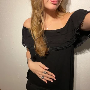 Svart offshoulder topp - Säljer en snygg svart offshoulder topp med spetsdetaljer. Perfekt för sommarens fester eller en kväll ute. Toppen har en lös passform och är superbekväm att bära. Den är i mycket bra skick och passar till både jeans och kjol.