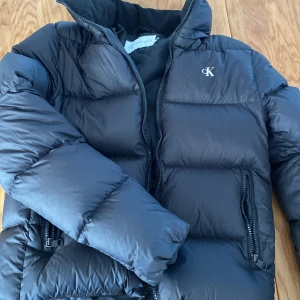 Svart pufferjacka från Calvin Klein  - Säljer en snygg svart pufferjacka från Calvin Klein  i storlek XS. Jackan har en dragkedja framtill och två praktiska fickor med dragkedjor. Perfekt för kalla vinterdagar och håller dig varm och stilren. Passar både till vardags och lite finare tillfällen.