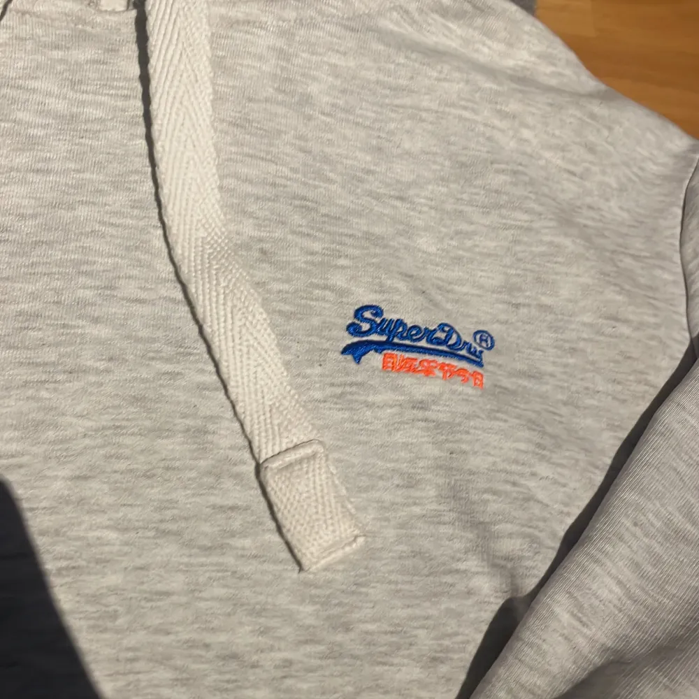 Säljer en snygg grå hoodie från Superdry i bra skick. Den har en klassisk design med justerbar huva och en liten broderad logga på bröstet. Perfekt för både höst och vår, Superbekväm och stilren!. Tröjor & Koftor.