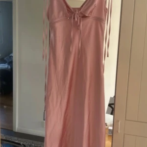 Rosa axelbandslös klänning - Säljer en superfin rosa klänning med axelbandslös design och knytning fram. Perfekt för sommarens fester eller en mysig dag på stan. Klänningen har en elegant och enkel stil som passar till många tillfällen. Den är i bra skick och redo för en ny ägare!
