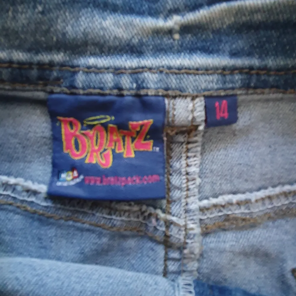 Säljer en supercool jeanskjol från Bratz med ett snyggt snörningsdetalj framtill och en färgglad Bratz-figur på sidan. Kjolen har en klassisk blå jeansfärg och två bakfickor. Perfekt för en avslappnad och trendig look!. Kjolar.