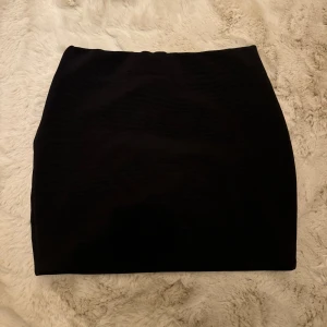 Svart ribbad kjol - Snygg svart ribbad kjol i kort modell. Perfekt för både vardag och fest! Den har en tight passform som framhäver figuren. Kjolen är i mycket bra skick och passar till alla säsonger. Ett måste i garderoben för den som älskar stilrena plagg.