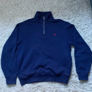 Mörkblå tröja från Polo Ralph Lauren - Säljer en snygg mörkblå tröja från Polo Ralph Lauren i storlek M. Tröjan har en halv dragkedja och det klassiska röda broderade logotypen på bröstet. Perfekt för både höst och vinter, och den är superbekväm att ha på sig. Passar till alla tillfällen!