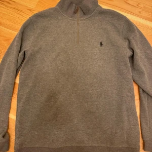  Ralph Lauren tröja - Säljer en stilren grå tröja från Polo Ralph Lauren i storlek L. Tröjan har en halv dragkedja och är perfekt för både vardag och lite finare tillfällen. Den är i mycket bra skick och har en klassisk passform. Perfekt för höst och vinter! Ej autentisk! Kan passa dig med storlek M