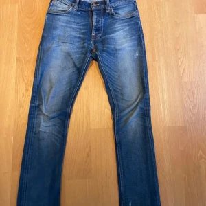 Blå jeans från Nudie Jeans - Säljer ett par snygga blå jeans från Nudie Jeans i bra skick. De har en klassisk femficksdesign och en snygg tvätt som ger en cool look. Perfekta för både vardag och fest! Passar bra till sneakers eller kängor.