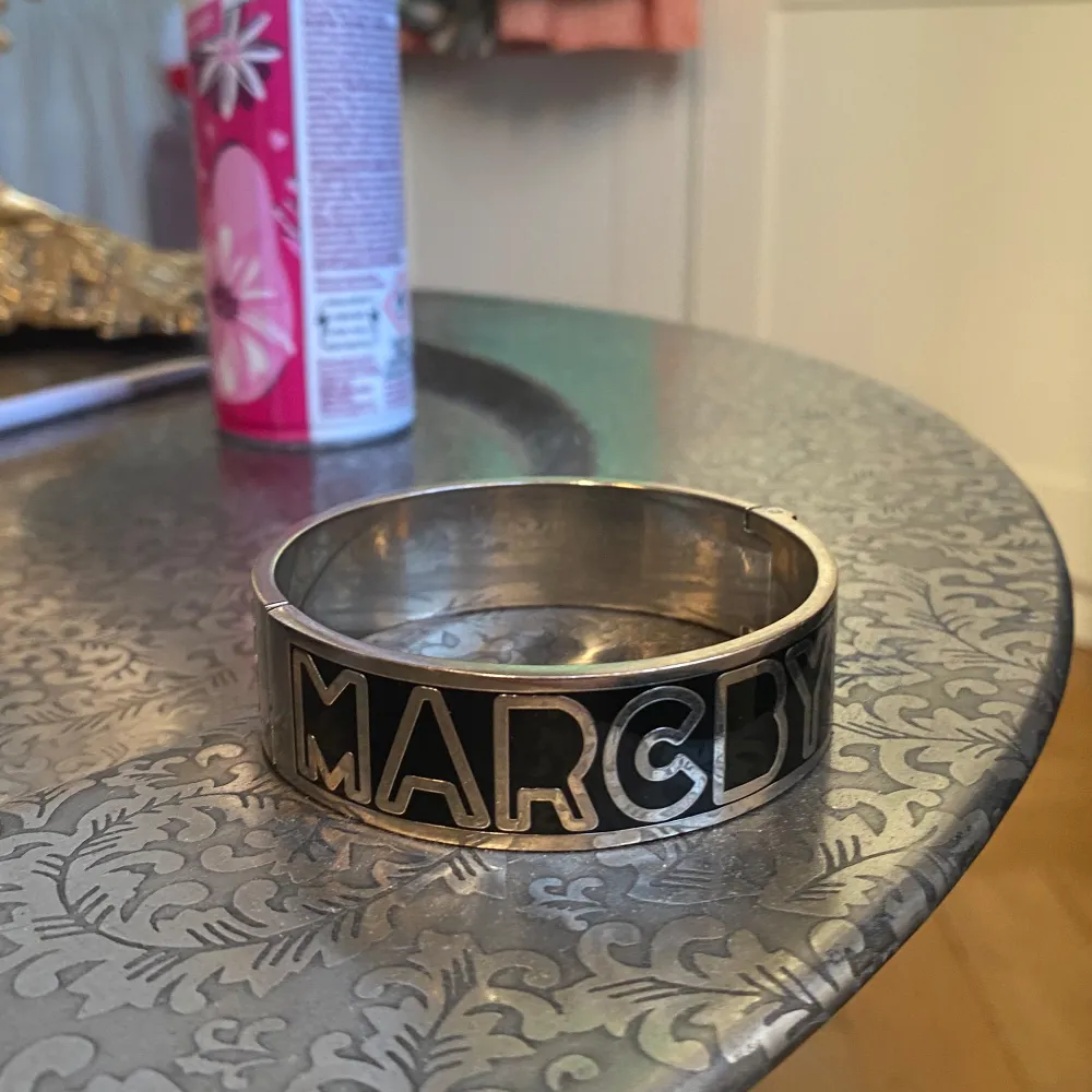Snyggt och stilrent armband i silverfärg från Marc by Marc Jacobs. Armbandet har en bred design med bokstäverna 'MARC BY MARC JACOBS' ingraverade runtom. Lite repigt på insidan av armbandet som ni ser på bild 2 annars väldigt bra skick!. Asusteet.