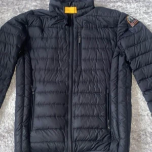 Svart lättviktsjacka från Parajumpers - Säljer en svart superlätt dunjacka från Parajumpers i mycket bra skick. Den har en snygg broderad logga på ärmen och praktisk dragkedja framtill. Perfekt för höst och vår när du vill hålla dig varm utan att känna dig tung. Passar både till vardags och lite finare tillfällen.