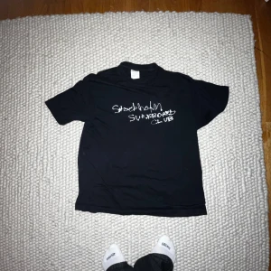 Stockholm Surfboard Club T-shirt - Säljer en svart t-shirt med texten 'Stockholm Surfboard Club' i vitt tryck. Perfekt för en avslappnad stil och passar bra till vardags. T-shirten har en normal passform och korta ärmar. Skön och enkel att matcha med jeans eller shorts.