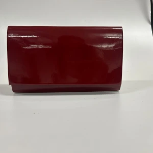 burgendy kuvertväska  - Snygg röd kuvertväska glansig. Perfekt för en utekväll eller fest. Enkel och stilren design som passar till många outfits. Väskan är i mycket bra skick och redo att användas för att ge din look det där lilla extra.