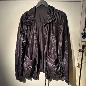 mörkblå vind/regnjacka från J.Lindeberg - Säljer en snygg mörkblå vindjacka från J.Lindeberg i M/L. Den har en cool, glansig finish och praktiska fickor framtill. Jackan är perfekt för blåsiga dagar och har en justerbar dragsko i nederkant. Passar både till vardags och lite mer uppklädda tillfällen. Den har använts men är i bra skick! Köpt för 2000kr på NK. Tveka inte att höra av dig om du har frågor eller vill ha fler bilder 