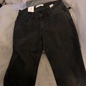 Svarta jeans från Stay - Säljer ett par svarta jeans från Stay i storlek S. De är i nytt skick och har en klassisk design med knapp och dragkedja framtill. Perfekta för både vardag och fest!