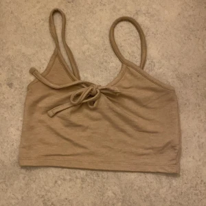 Beige linnetopp från Bik Bok - Säljer en söt beige linnetopp från Bik Bok i storlek XS. Toppen har smala axelband och en knytning framtill som ger en fin detalj. Perfekt för sommardagar eller som ett lager under en tröja. Materialet känns mjukt och bekvämt mot huden.